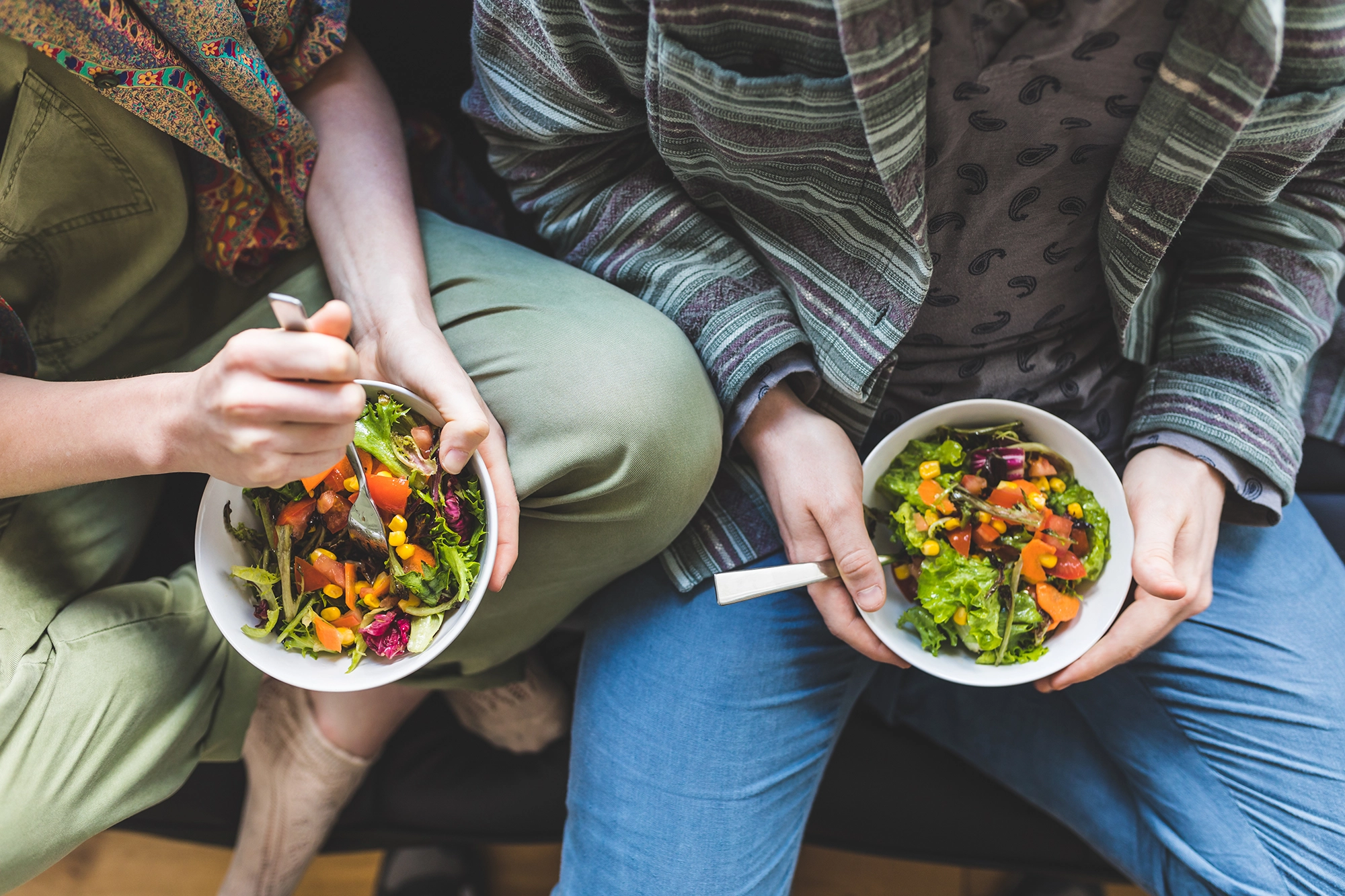 An overhead shot of a couple sitting on the couch, each holding a salad in their lap.